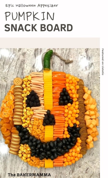 Pumpkin shaped food appetizer snack board tray on a granite counter made of orange veggies, fruits, crackers, cookies, popcorn and cheese. A carved pumpkin face is shaped from black olives, berries and dried figs. 