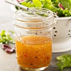 Jar of Italian dressing next to a bowl of salad.