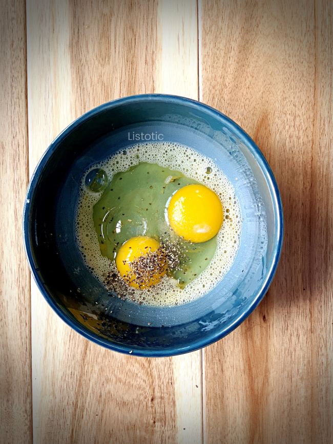 The start of scrambled eggs. Two eggs broken into a bowl with salt and pepper.