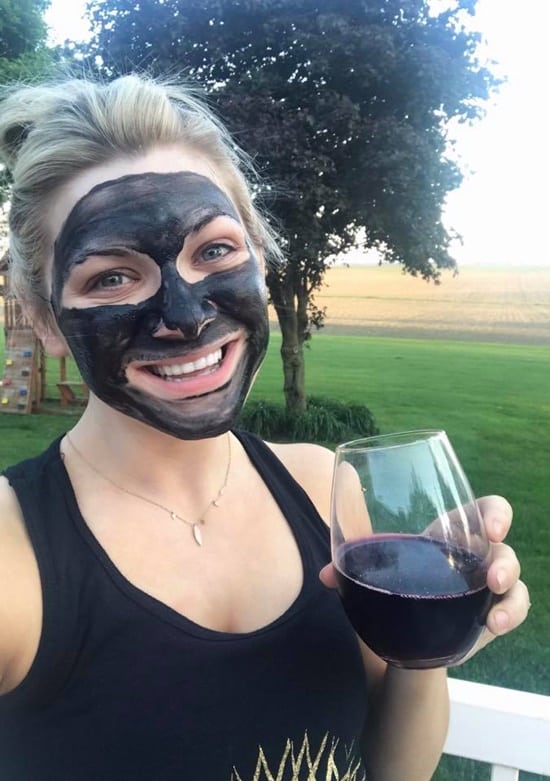Woman with wine glass working on skin care 101 with bamboo charcoal detoxifying mask to leave skin baby soft.