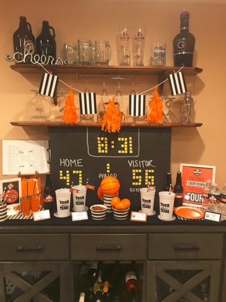 DIY scoreboard backdrop on a table decorated with Basketball themed centerpieces and March Madness party food.