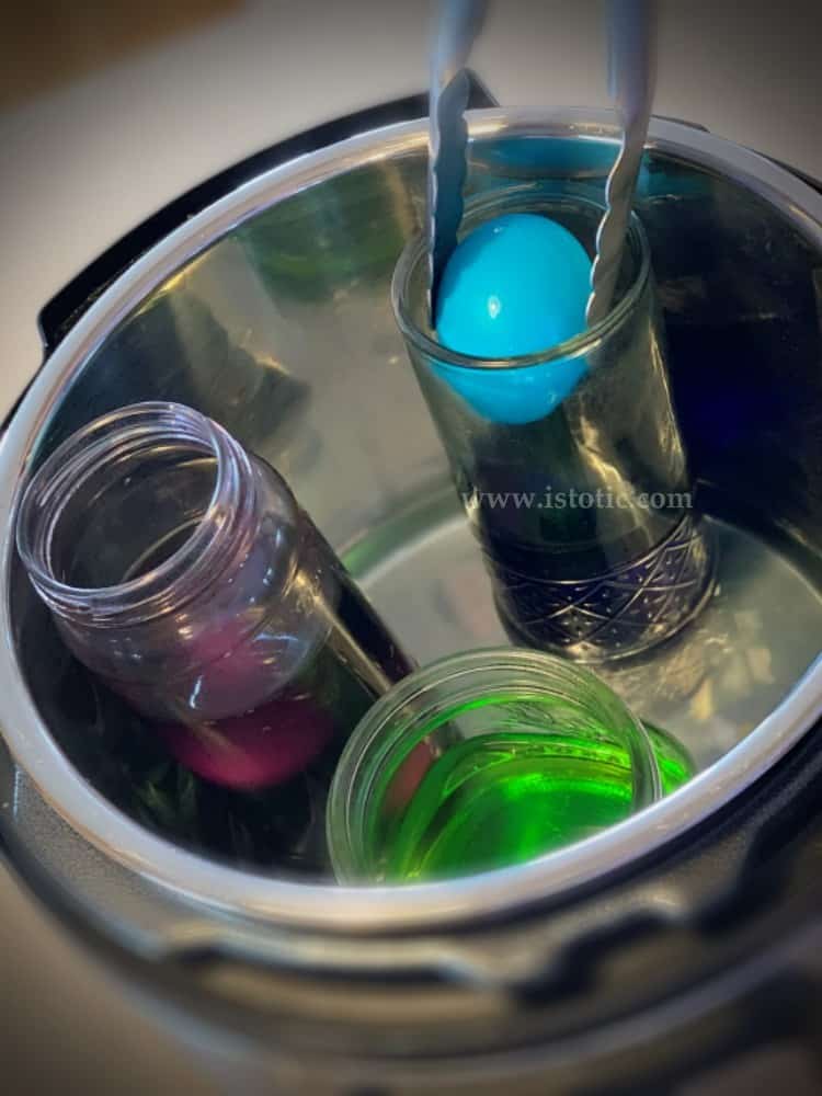 Tongs removing a bright blue hardboiled Easter egg from a mason jar filled with food coloring and vinegar in the instant pot. 