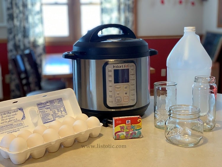 Materials for dyed Easter eggs in the instant pot kitchen counter with box of food coloring, carton of eggs, three mason jars, bottle of white vinegar and six quart instant pot.