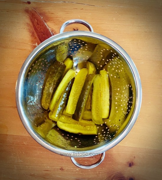Crisp dill pickles in a silver strainer on a rustic wood table.