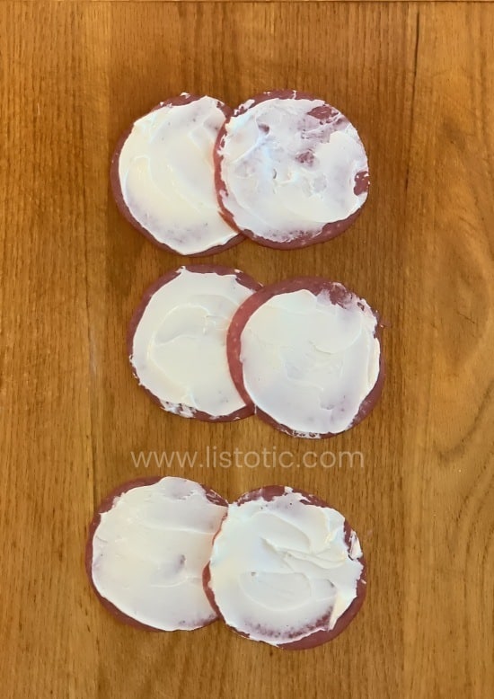 Slices of buddings dried beef smeared with cream cheese over-lapped on a wooden cutting board.