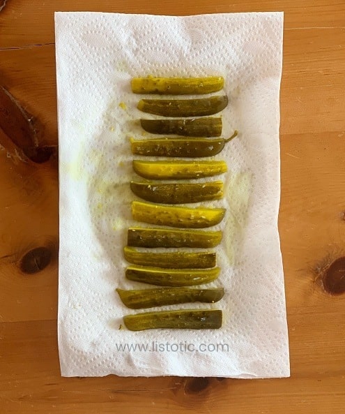 Roll of crisp dill pickle spears lined up on a white paper towel - ready to make dill pickle roll up recipe.