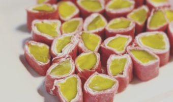 Green dill pickles wrapped in cream cheese and dried beef on a white appetizer plate.