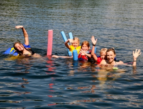 Family swimming in a lake with life jackets and noodles.