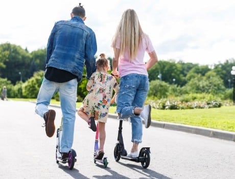 Family riding their scooters in unison, enjoying the park.