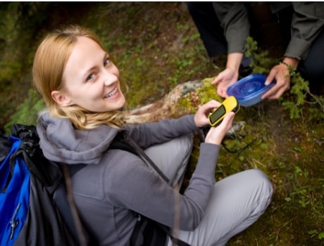 Woman using GPS to search for geocaches. A geocache is found!