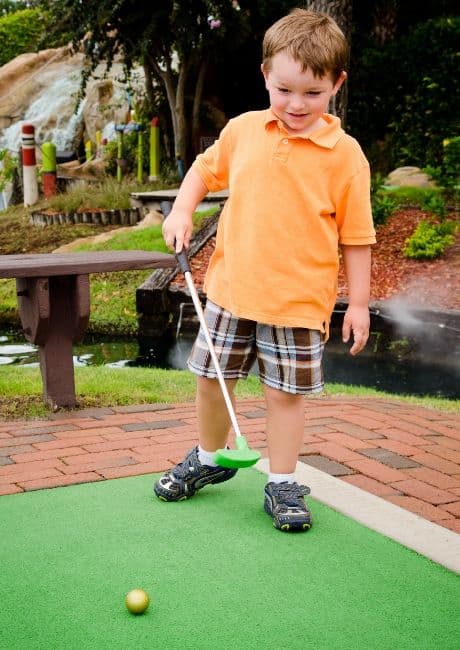 Young boy playing miniature golf.