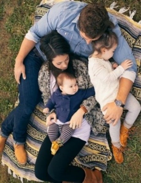 above shot taken of family of four comfortably laying on a patterned blanket together on a fall afternoon wearing jeans and casual clothing for outdoor family portraits. 