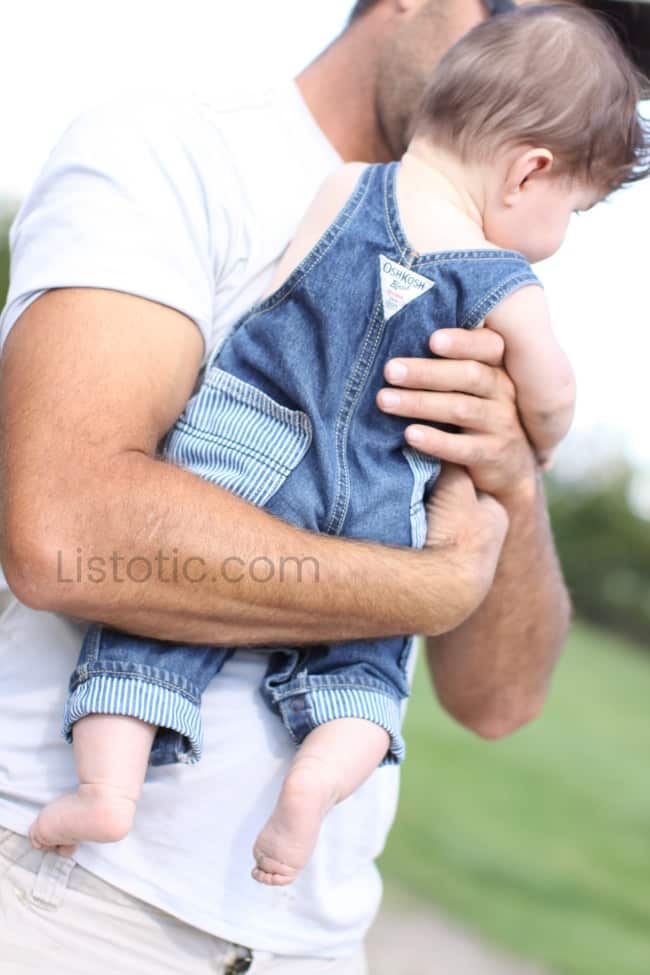 Muscular arm of a man holding baby boy wearing bib overalls and bare feet