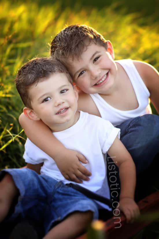 Two boys wearing white shirt and jeans sitting in tall grass smiling