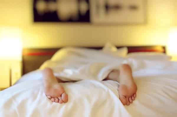 Exhausted woman laying in bed with just feet showing under a bed cover.