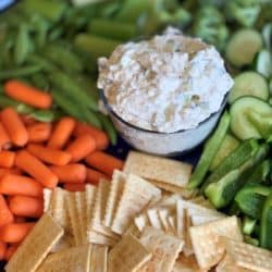 Crunchy fresh Cucumbers, pepper, carrots, celery, broccoli and sugar snap peas on a tray with crackers with a creamy cucumber dill veggie dip in the center.