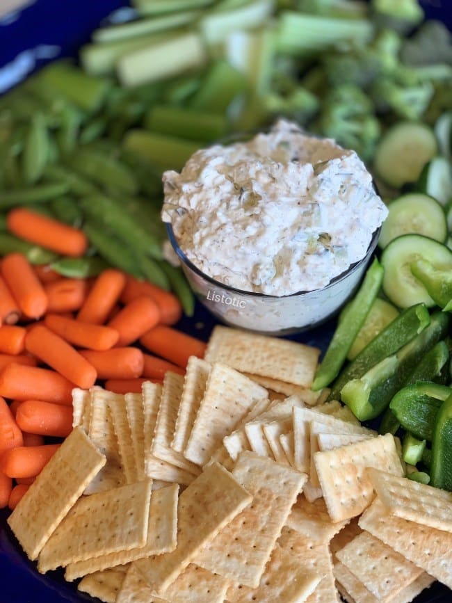 Crunchy fresh Cucumbers, pepper, carrots, celery, broccoli and sugar snap peas on a tray with crackers with a creamy cucumber dill veggie dip in the center. 