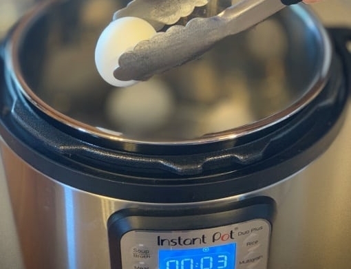 Instant pot hard boiled egg coming out of the Instant Pot in tongs.