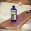 Bath tub tray made from rustic live edge wood slab on a bath tub of foaming bubbles. Bottle of wine and wine glass with a lit candle.