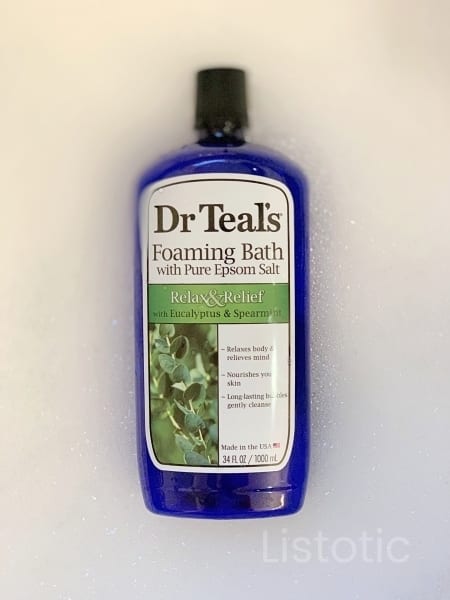 Blue plastic bottle of Dr. Teal’s Foaming Bubble bath floating on top a full bath tub of foamy bath bubbles.