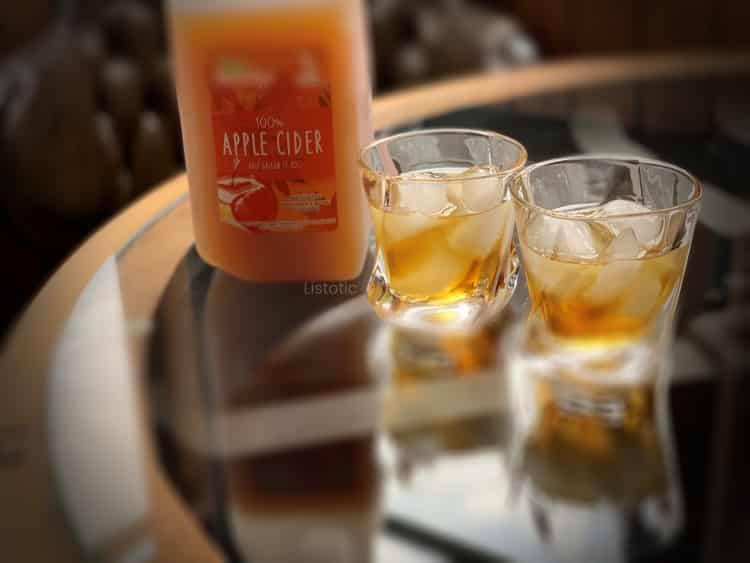 Two glasses sitting on a table half filled with fireball and apple whiskey. A half gallon jug of homemade apple cider sitting behind the glasses on the glass top dinning room table. 