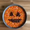 Round metal baking pan of Halloween candy corn fudge shaped like a pumpkin with chocolate chip eyes and mouth dessert sitting on a table.