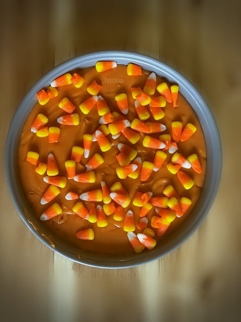 Round baking pan filled with creamy candy corn peanut butter fudge and topped with more candy corn candies before cooling.