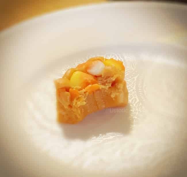 Single piece of candy corn peanut butter fudge with a bite take out of it sitting on a white plate. 