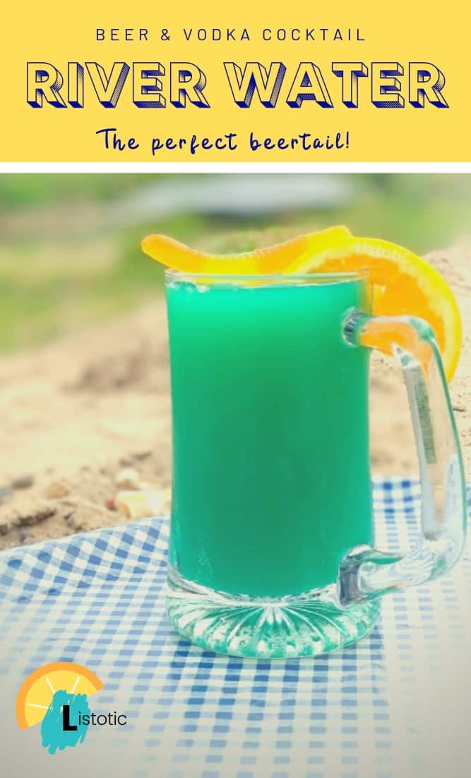 Pinterest image of a blue green colored cocktail with a gummy worm and orange slice garnished on a beer mug on a blue and white gingham metal tray on a sandy river bank on a summer day. 