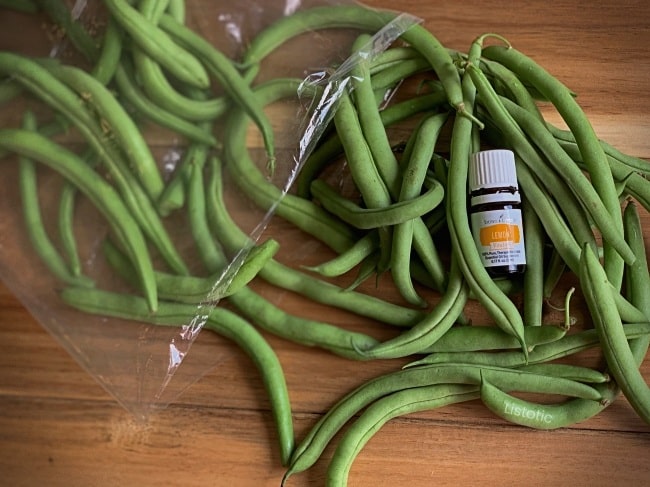 Fresh green beans on cutting board with a bottle of Young Living Lemon Vitality essential oil.