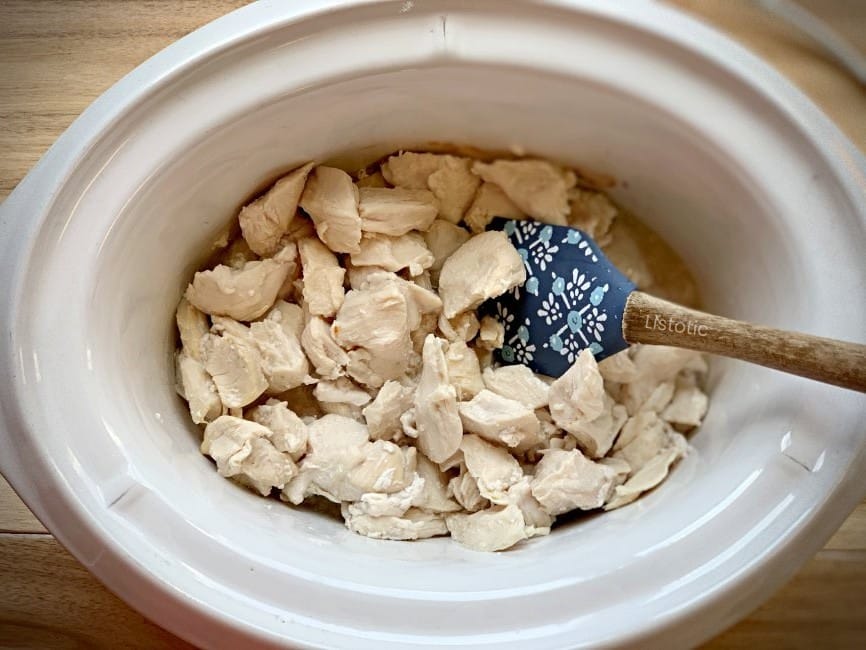 Bite sized chicken being stirred in crock pot for Orange Chicken crock pot recipe.