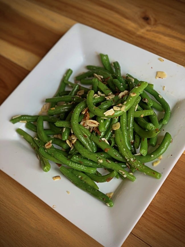 White plate with fresh green beans and slivered almonds.