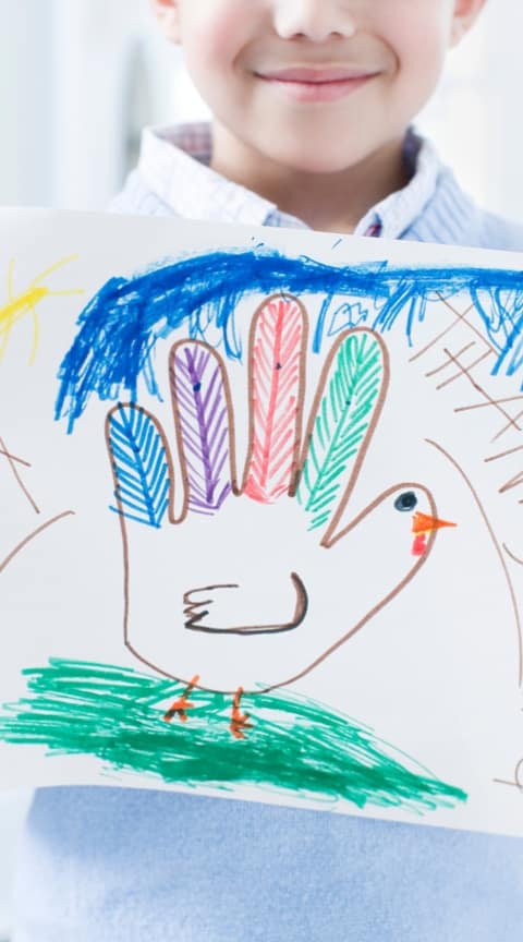 Child holding a drawing of a turkey made with bright colored markets for Thanksgiving.