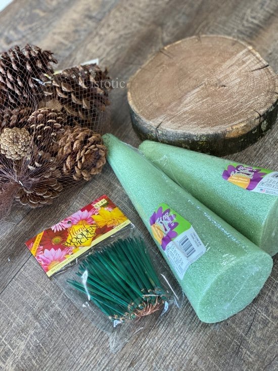 materials of foam floral cone wood slab, pinecones and floral picks needed to create a diy pinecone tree. 