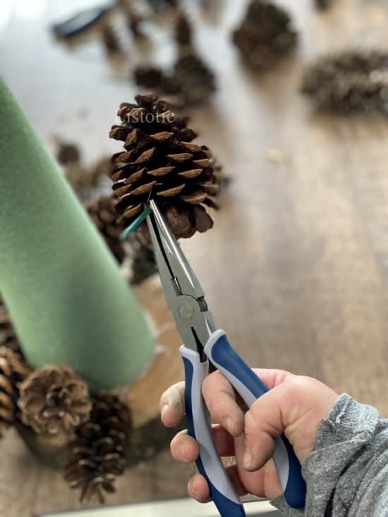 needle nose pliers holding a pinecone with floral pick attached 