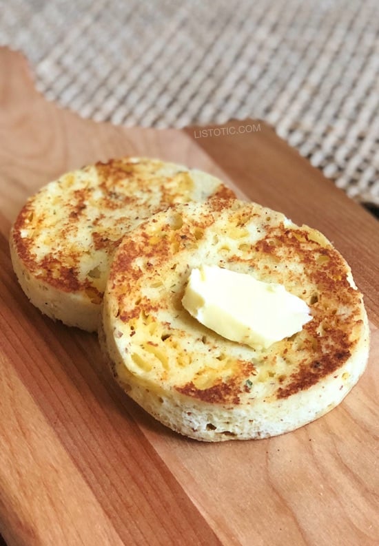 Two pieces of toasted round bread topped with butter on a wood cutting board.