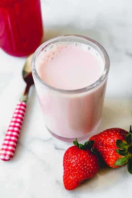 Glass of homemade strawberry milk and fresh strawberries on a counter