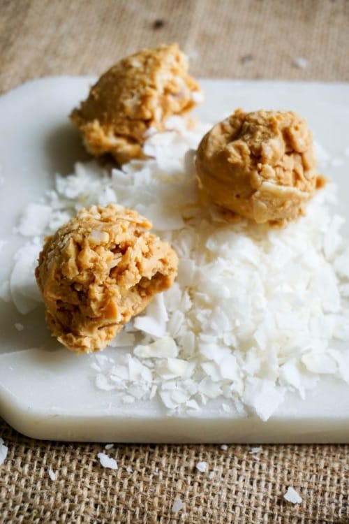 Three peanut butter balls sitting on a white tray with coconut flakes.