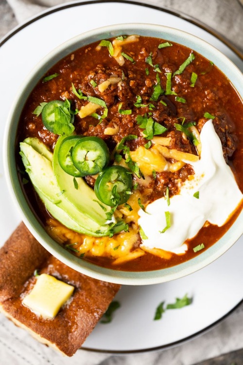 Hearty chili garnished with jalapeno slices, avocado, sour cream and a side of keto cornbread topped with melted butter.