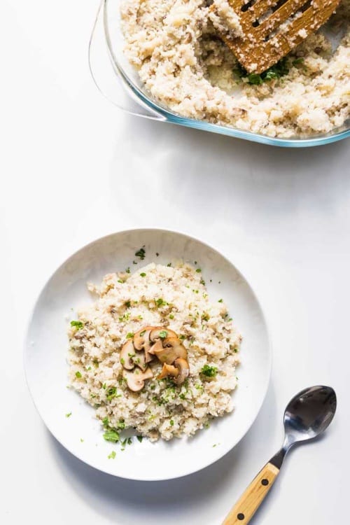 A white bowl filled with creamy mushroom risotto topped with parsley and garnished with sliced sautéed mushrooms for Keto minded person.