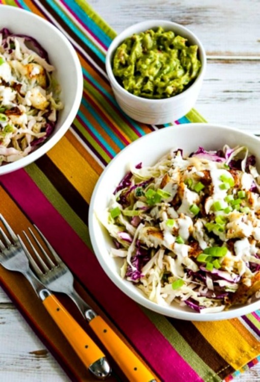 Fiesta themed table with a white bowl containing Fish Taco cabbage garnished with green onions and served with a dish of guacamole.