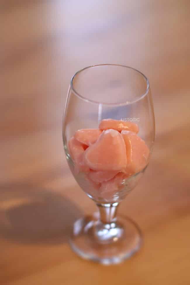 Glass half full of frozen strawberry milk ice cubes 