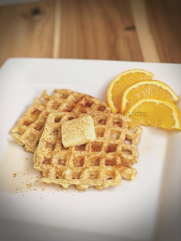 Low carb stacked cheesy flour-free waffle topped with syrup and melted butter on a white plate garnished with fresh orange slices.