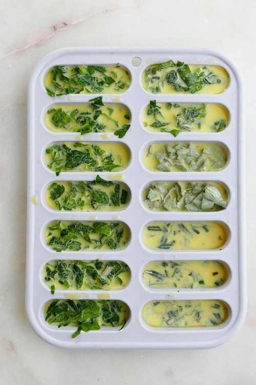 White Ice cube tray filled with oil and a variety of herbs ready to be frozen. 