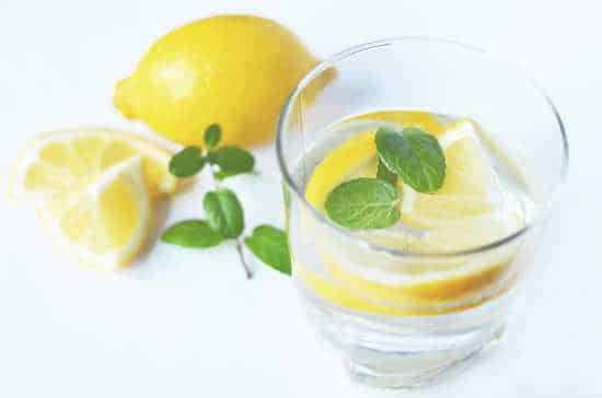 A glass of water with quartered lemon wedges and sprig of herbs.