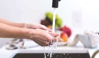 A person washing food or hands under running water in a kitchen with blurred background.