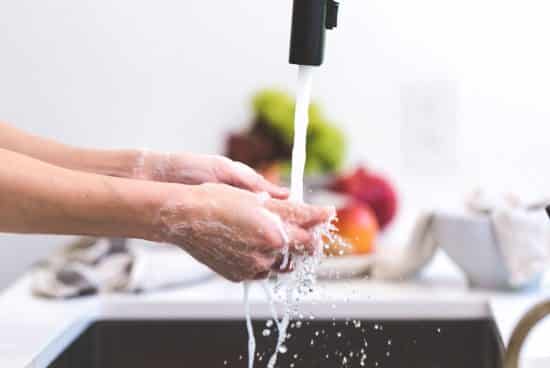 A person washing food or hands under running water in a kitchen with blurred background. 