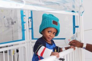 A toddler depicted in a cradle wearing a blue Love Your Melon beanie.