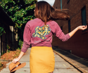 Woman wearing a t-shirt with a turtle print on the back labelled “Shelly Cove.”