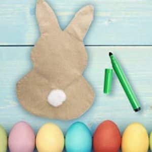 A customizable bunny yard flag on a table with a green marker and colorful Easter eggs placed beside it.